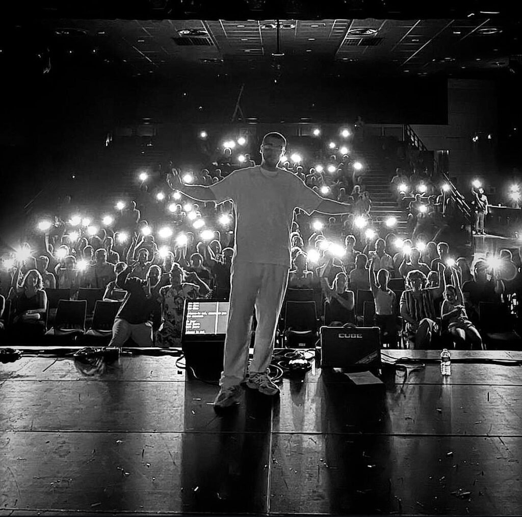Le rappeur montalbanais Ziano sur scène devant un public allumant leurs lumières de téléphone.