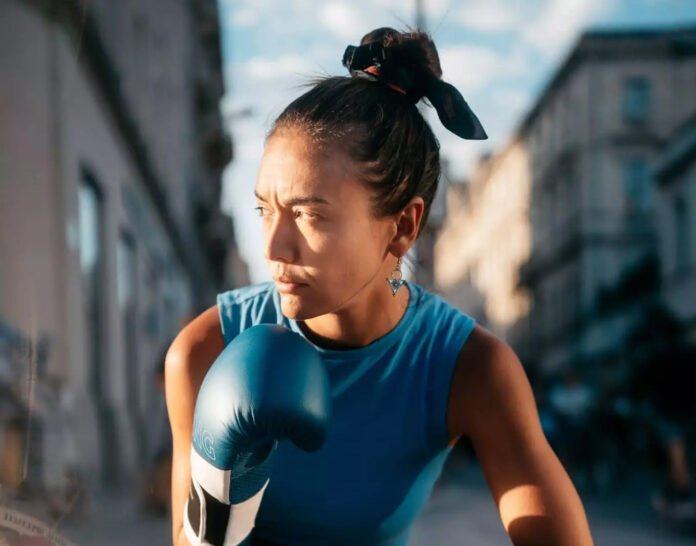 Jeune femme boxeuse en gants bleus regard déterminé spectacle L'odeur de la guerre Montauban 2026